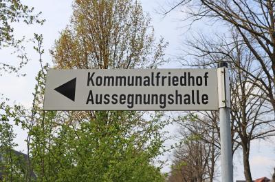 Wegweiser Schild mit Richtungspfeil links und schwarzem Text Kommunalfriedhof Aussegnungshalle